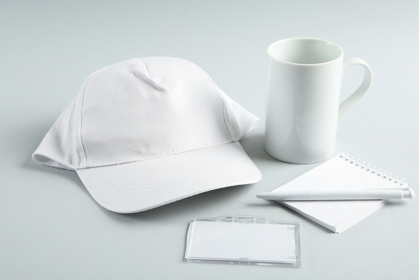 White promotional hat, mug, notebook, and pen arranged as branded gift ideas for client appreciation.